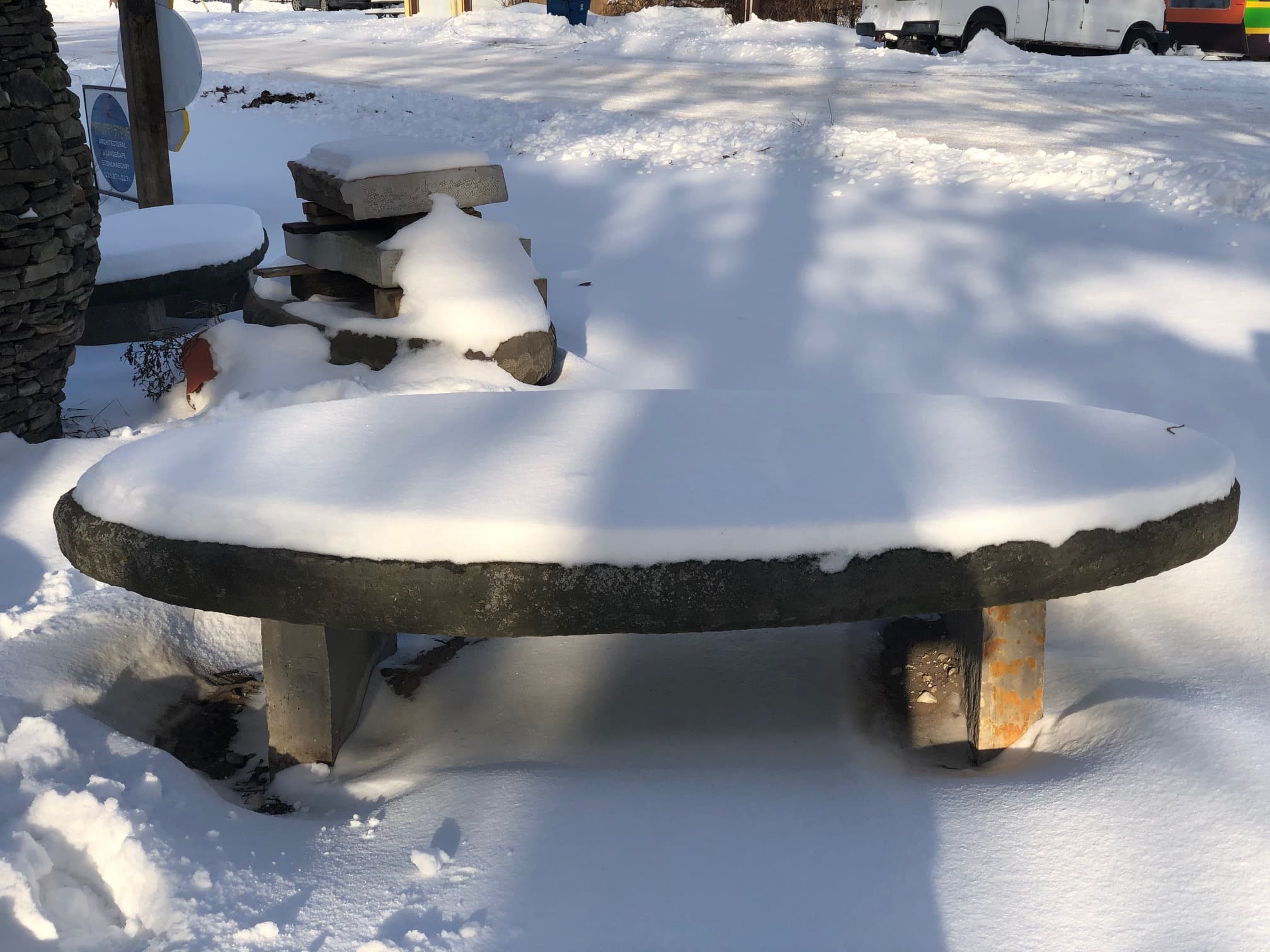Snow-covered elliptical stone bench in winter.