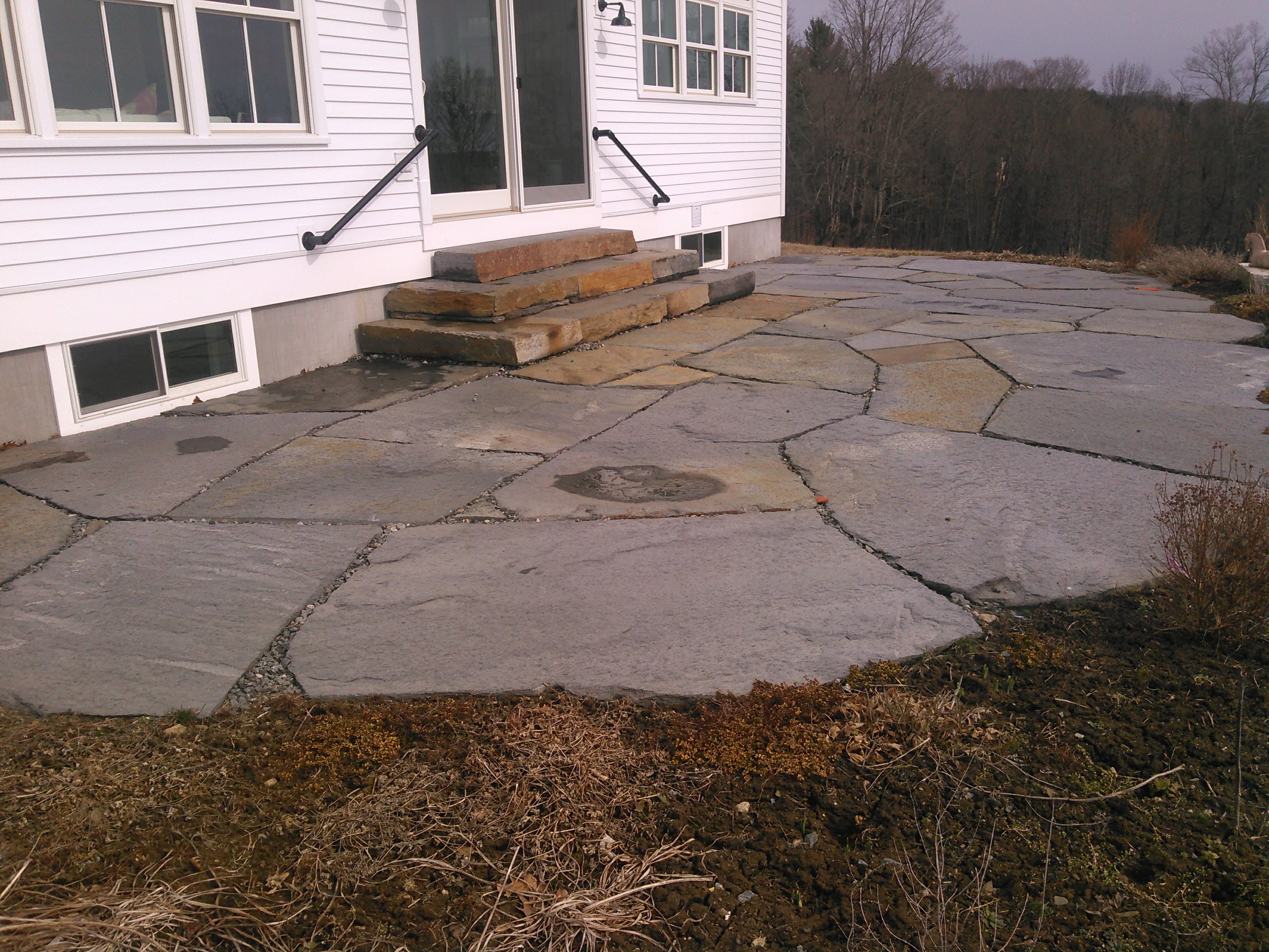Finished flagstone patio with stone steps at a clapboard house.