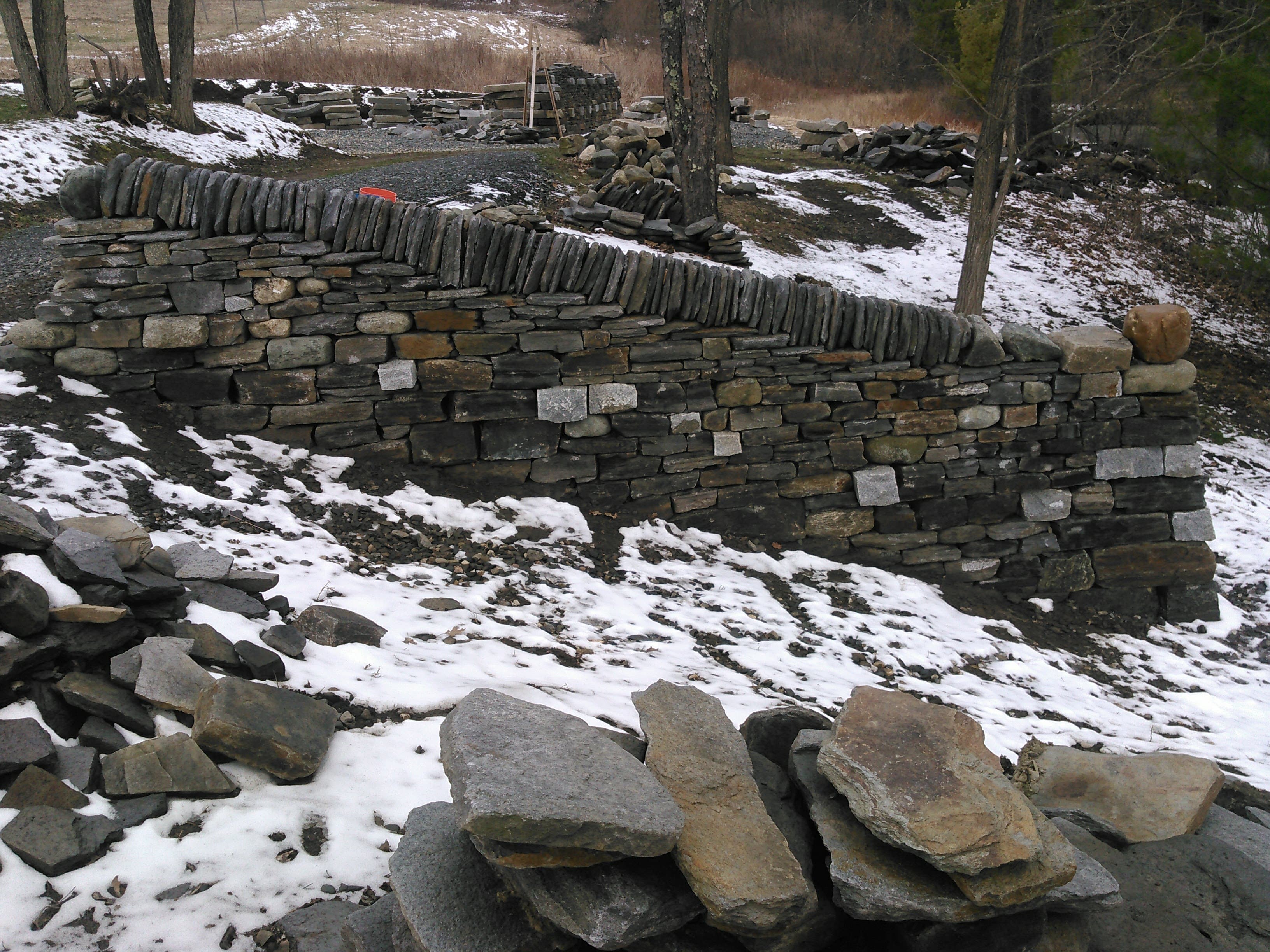Freestanding dry stone walls in progress on a sloped site.