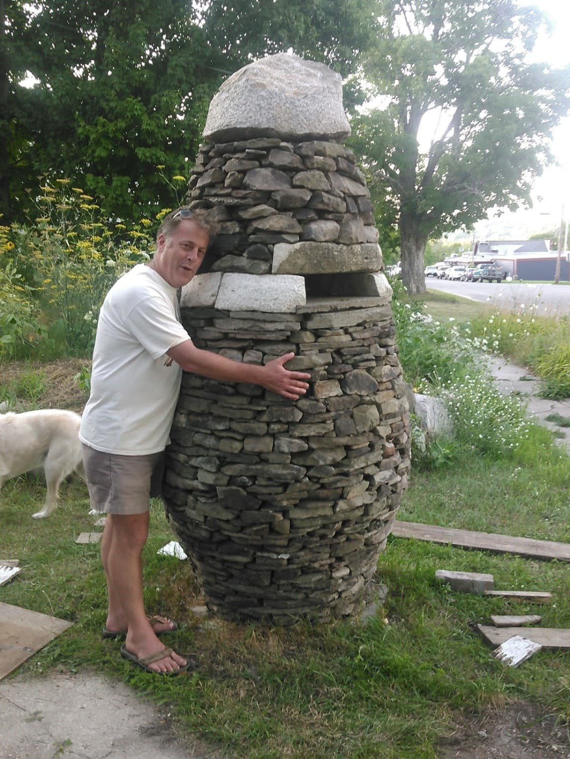 A man hugging a tall urn-shaped dry stone cairn.