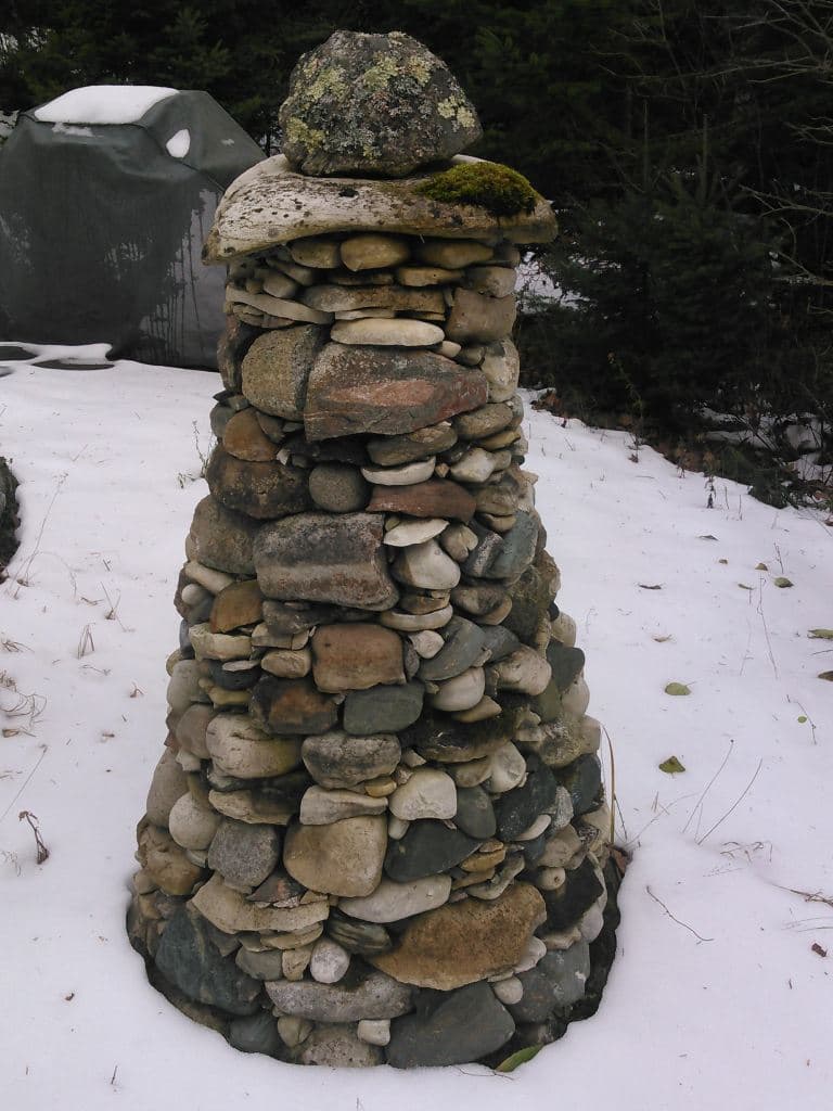 Conical dry stone cairn beside a shingled building.