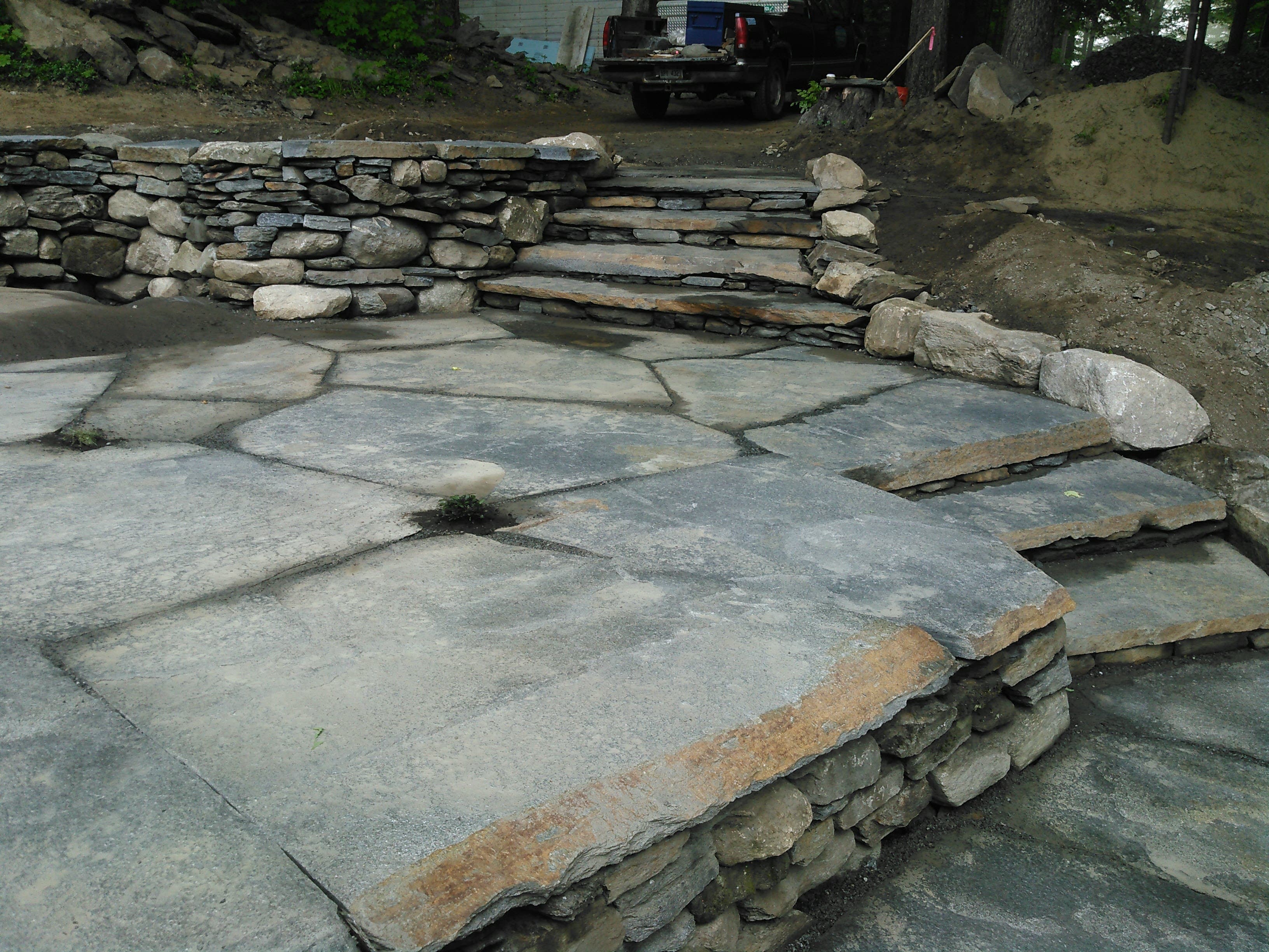 Slab steps and flagstone paving stepping down beside a dry stone retaining wall.